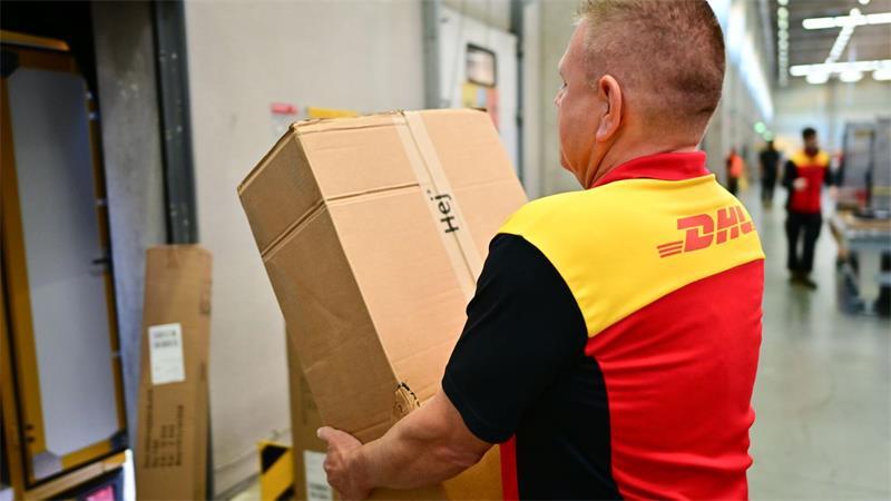Ein Paketbote schleppt in einem DHL-Standort ein schweres Paket. (Archivbild)