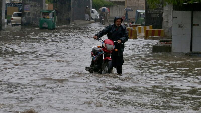 Ein Pakistaner watet nach starken Regenfällen mit seinem Motorrad durch eine überschwemmte Straße in Peschawar.