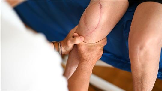Ein Physiotherapeut behandelt das Bein einer Patientin. In diesen Branchen fehlen die meisten Fachkräfte im Gesundheitswesen.