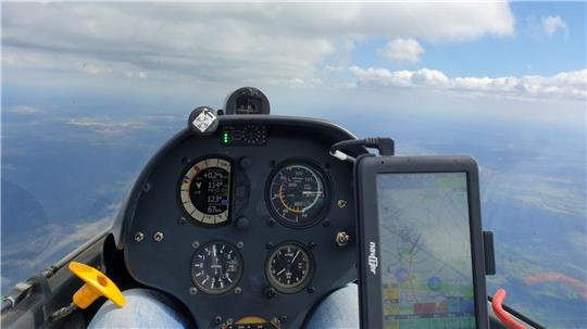 Blick eines Piloten aus dem Segelflieger auf die Lüneburger Heide. Im Vordergrund ist ein GPS-System, oben ist eine Wolkenstraße.