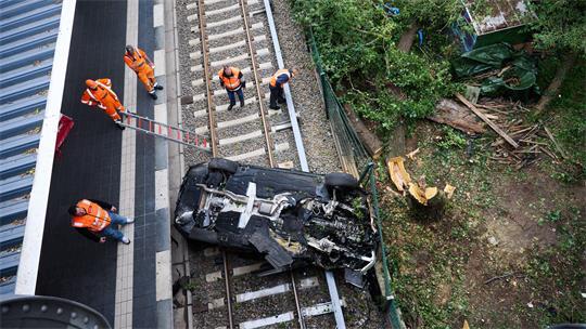 Ein Pkw liegt bei der Bornholmer Brücke im Gleisbett, während Mitarbeiter des THWs und der Bahn daneben stehen. 