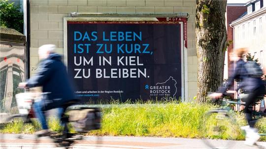 Ein Plakat mit der Aufschrift „Das Leben ist zu kurz, um in Kiel zu bleiben“ hängt an einem Haus.