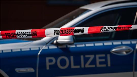 Ein Polizeiauto steht hinter einem Absperrband der Polizei.