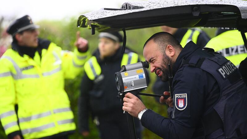 Ein Polizist kontrolliert mit einem Messgerät die Geschwindigkeit von Fahrzeugen in einer 30er-Zone.