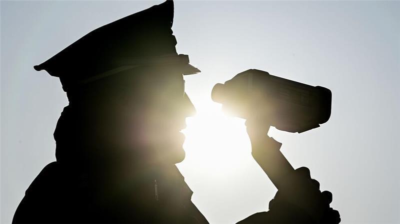 Ein Polizist misst mit einer Laserpistole die Geschwindigkeit vorbeifahrender Fahrzeuge. 
