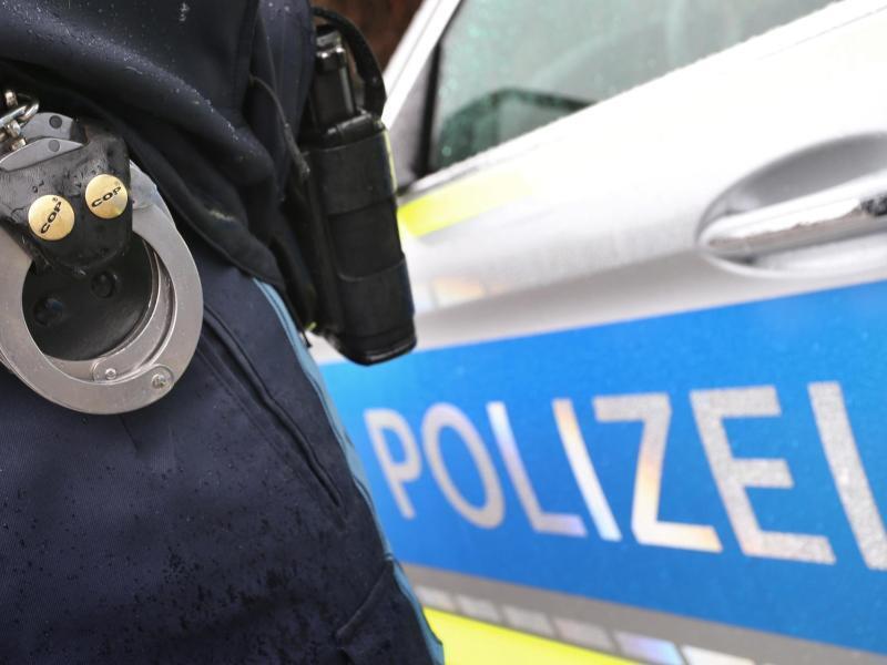 Ein Polizist mit Handschellen und einer Pistole am Gürtel steht vor einem Streifenwagen. Foto: Karl-Josef Hildenbrand/dpa