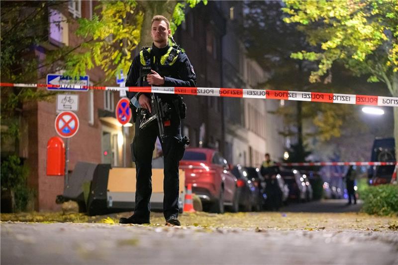 Ein Polizist mit einer Maschinenpistole sichert am Sonntagabend den abgesperrten Tatort im Phoenix-Viertel in Harburg ab. Foto: Jonas Walzberg/dpa