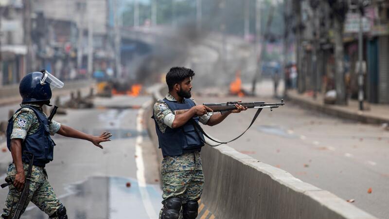 Bangladesch: Regierungschefin tritt nach Protesten zurück Ein Polizist richtet seine Waffe auf Demonstranten: Bei den Protesten sind Medienberichten zufolge bereits Hunderte Menschen ums Leben gekommen.