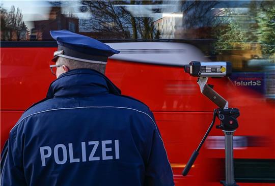 Ein Polizist steht mit einer Laserpistolean einer Straße und misst die Geschwindigkeit.