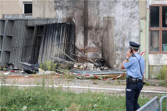 Ein Polizist steht vor den Wrackteilen eines Kleinflugzeugs nach dem Absturz auf eine Lagerhalle.