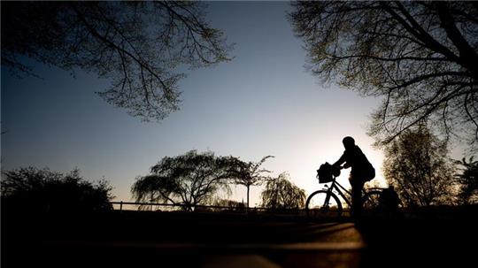 Ein Radfahrer fährt kurz vor Sonnenuntergang auf einem Radweg an der Alster entlang.