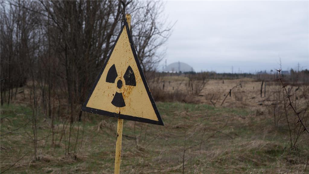 Ein Radioaktivitäts-Warnzeichen, im Hintergrund das Kernkraftwerk Tschernobyl, a...