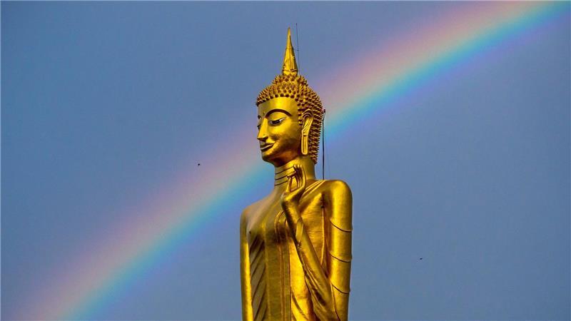 Ein Regenbogen ist hinter der stehenden Buddha-Statue Luang Pho Yai des Wat Buraphaphiram in Roi Et, Thailand, zu sehen.