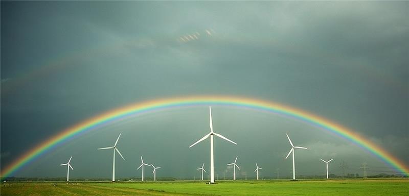 Ein Regenbogen spannt sich über grünen Feldern und Windkraftanlagen vor grauen Regenwolken bei Wilster (Schleswig-Holstein). Foto: Christian Charisius/dpa