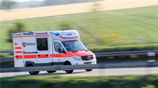 Ein Rettungswagen fährt mit Blaulicht über eine Landstraße.