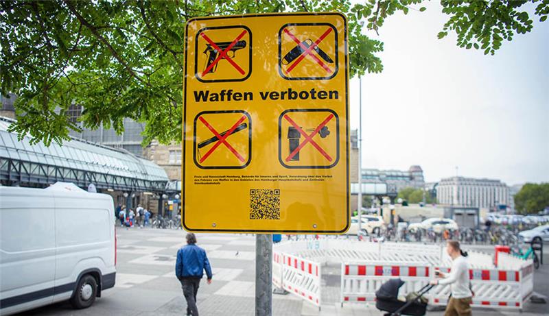Ein Schild („Waffen verboten“) informiert mit Piktogrammen vor dem Hamburger Hauptbahnhof über die neu eingerichtete Waffenverbotszone. Foto: Gregor Fischer/dpa