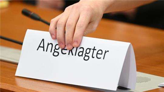 Ein Schild mit der Aufschrift „Angeklagter“ wird auf die Gerichtsbank gestellt.