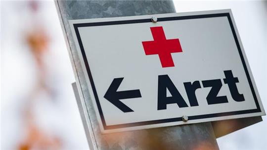 Ein Schild mit der Aufschrift „Arzt“ hängt an einer Straßenlaterne.