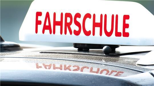 Ein Schild mit der Aufschrift „Fahrschule“ ist auf einem Fahrschulauto befestigt. 