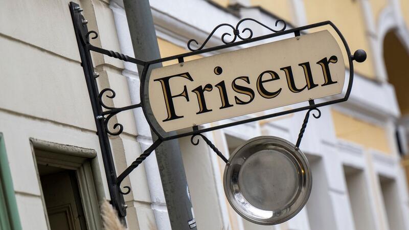 Ein Schild mit der Aufschrift „Friseur“ hängt an einem Gebäude.