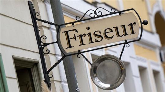 Ein Schild mit der Aufschrift „Friseur“ hängt an einem Gebäude.