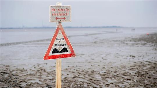 Ein Schild mit der Aufschrift „Vorsicht Jadebusen“ steht im Wattboden am Strand von Dangast.