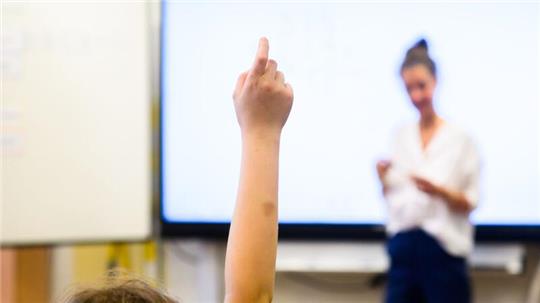 Ein Schüler meldet sich per Handzeichen in einem Klassenraum.