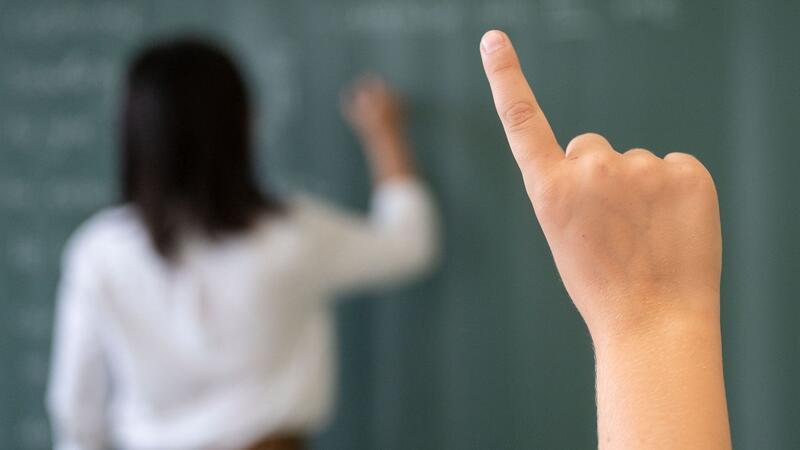 Ein Schüler meldet sich, während die Lehrerin an die Tafel schreibt.