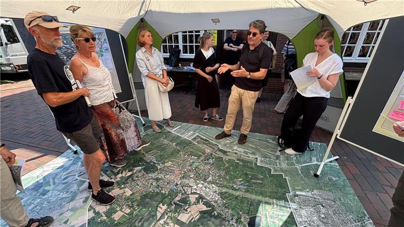 Viele Parkplätze in Buxtehudes Innenstadt: Planer hält das für „verrückt“ Ein Stadtplan am Fußboden zeigt die Altstadt und die Bahnhofstraße: Stadtplaner Dr. Lars Bölling (Zweiter von rechts) begrüßt Teilnehmer und Teilnehmerinnen des Stadtteilspaziergangs in einem Pavillon auf dem Petri-Platz.