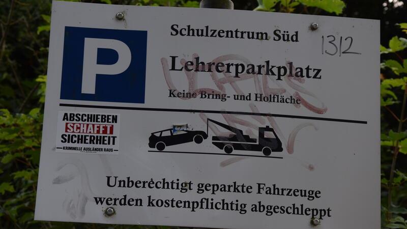 Ein Sticker mit rechtsextremer Parole klebt auf dem Schild am Lehrerparkplatz. Slogan und Piktogramm bilden eine Komposition.