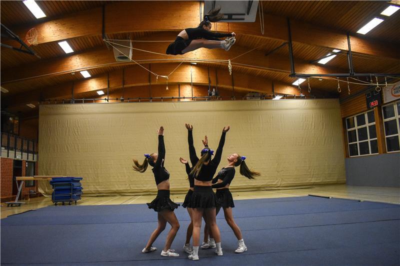Hollywood-Glitzer: Wiepenkathen tritt in den USA und gegen Klischees an Eine Cheerleaderin macht einen „Pike Pretty Basket“ und fliegt in der Luft, vier andere auf einer Bodenmatte stehen bereit, um sie aufzufangen.