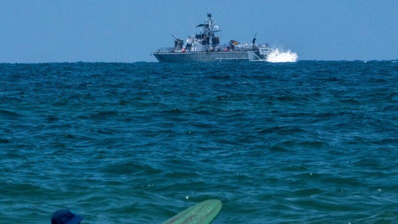 Ein Surfer wartet auf eine Welle, während ein israelisches Marineschiff im Mittelmeer vor der Küste von Hadera patrouilliert.