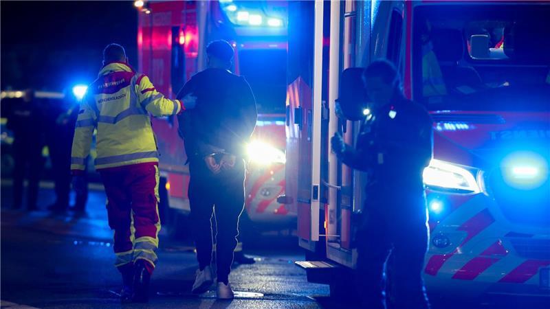 Ein Tatverdächtiger in Handschellen wird nach Schüssen in Mönchengladbach von einem Sanitäter zu einem Rettungswagen gebracht.