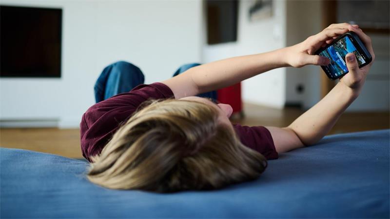 Ein Teenager guckt auf ein Handy, während er auf einer Matratze liegt (gestellte Szene).