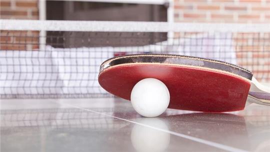 Ein Tischtennisball und ein Schläger liegen auf einer Tischtennisplatte.