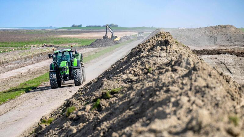 Ein Traktor fährt an einer Baustelle an einem Deich vorbei.