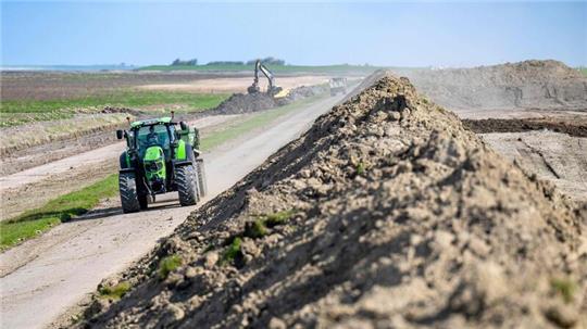 Ein Traktor fährt an einer Baustelle an einem Deich vorbei.