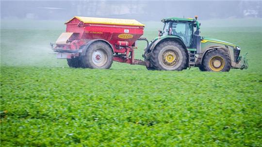 Ein Traktor fährt mit einem Streuwagen über ein Feld und bringt Dünger aus.