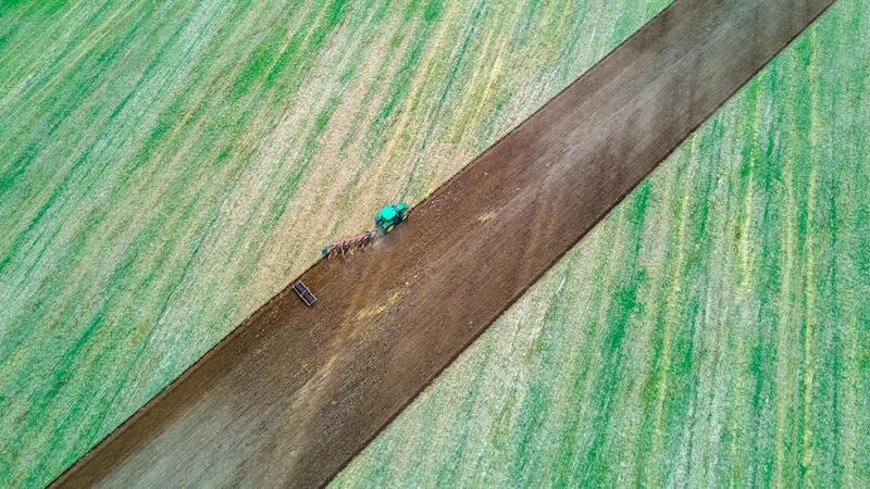 Ein Traktor zieht Pflug und Egge über ein abgeerntetes Feld.