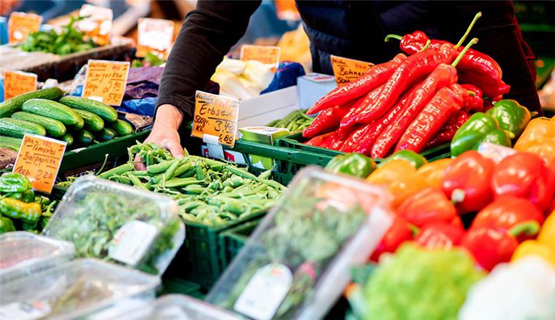 Ein Verkäufer greift an einem Obst- und Gemüsestand auf dem Wochenmarkt in eine Kiste mit Erbsen. Symbolfoto: Hauke-Christian Dittrich/dpa