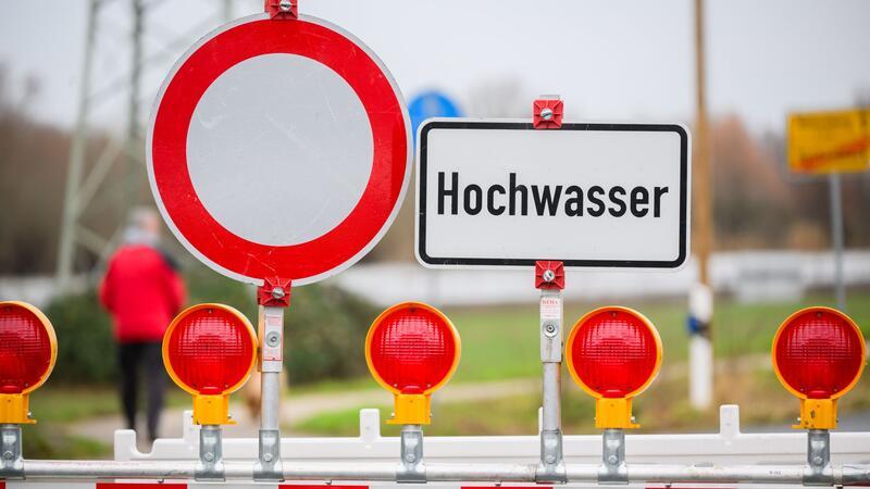 Ein Warnschild „Hochwasser“ steht an einer Straßensperre.