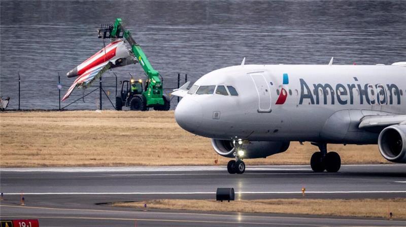 Ein Wrackteil wird am Potomac River auf einen Truck geladen, während ein Flugzeug vom Ronald Reagan Washington National Airport abhebt.