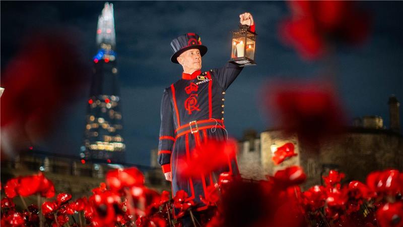 Ein Yeoman Warder (Beefeater) des Tower of London hält eine Laterne bei einer Ausstellung von Keramik-Mohnblumen im Tower anlässlich des Armistice Day.