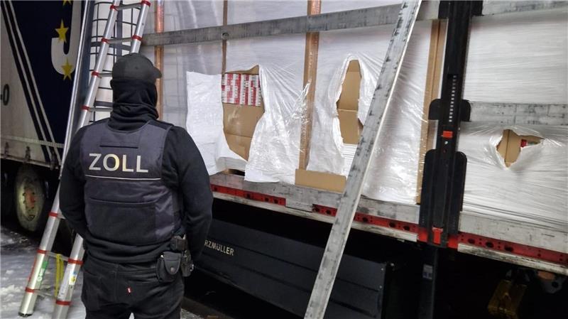 Ein Zöllner steht vor einem mit Zigaretten beladenem Lkw.