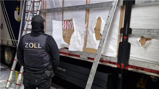 Ein Zöllner steht vor einem mit Zigaretten beladenem Lkw.