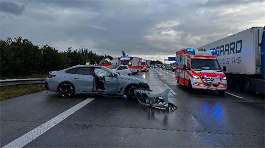 Ein beschädigter Pkw steht nach der Kollision auf der regennassen A1; Einsatzkräfte sichern die Unfallstelle. 