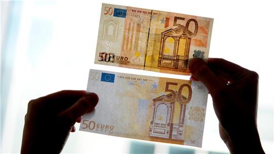 Ein echter und ein falscher Fünfzig-Euro-Schein werden gegen das Licht gehalten.