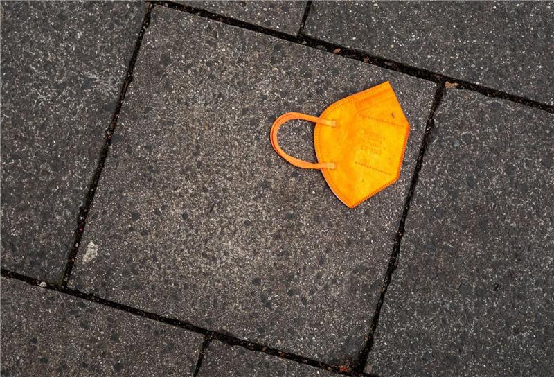 Sachverständige legen Evaluierung der Corona-Maßnahmen vor Ein gebrauchter orangefarbener Mund-Nasen-Schutz liegt auf dem Gehweg.