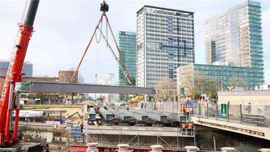Ein großer Lastenkran hebt tonnenschwere Stahlträger zur Erneuerung der Berlinertordammbrücke über der Straße Bürgerweide und den Bahngleisen ein.