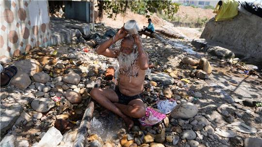 Ein heiliger Mann kühlt sich an einem heißen Tag in der indischen Stadt Jammu mit Wasser ab.